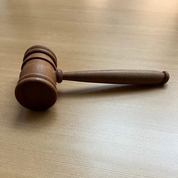 A dark brown wooden gavel lying on a lighter brown wooden office table