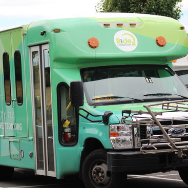 A Ride Connection shuttle bus, painted in shades of green with the Ride Connection logo prominently displayed on the front and sides of the shuttle bus.