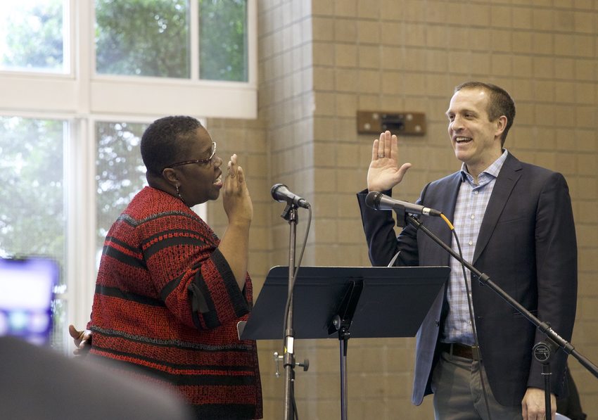 Auditor Brian Evans smiles and raises his hand as he is sworn into office.