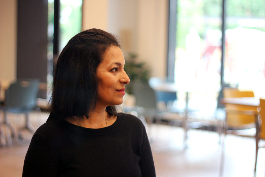 Woman with black hair and shirt in profile, sitting in an indoor space