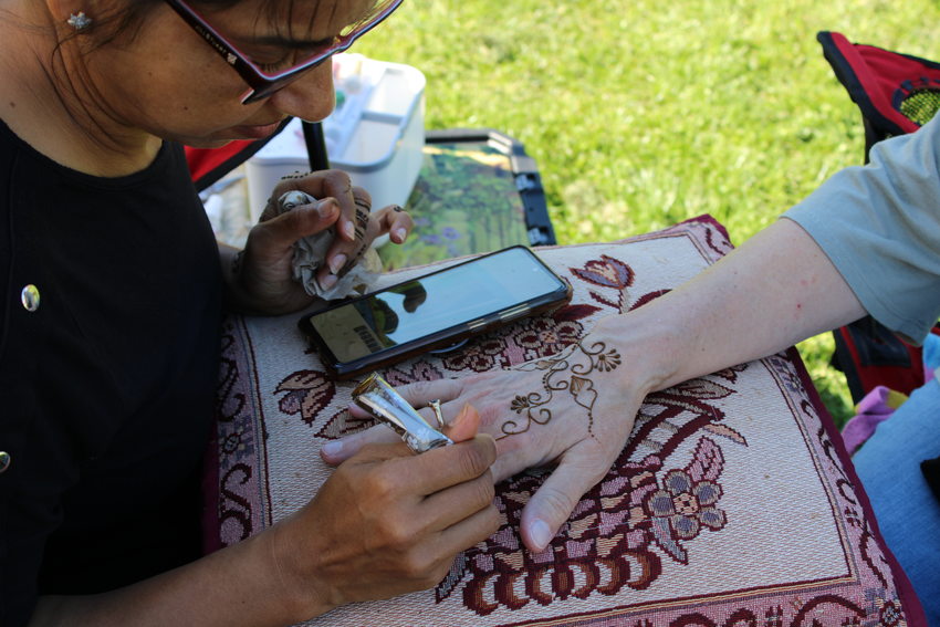A person does henna on another person's hand as it rests on an embroidered pillow
