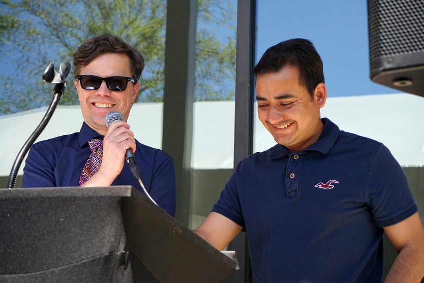 Two men standing at a podium and smiling. The one on the left is holding a microphone.