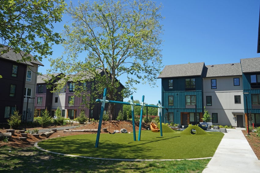 Grassy plaza between multifamily housing buildings with a swingset in the middle. 