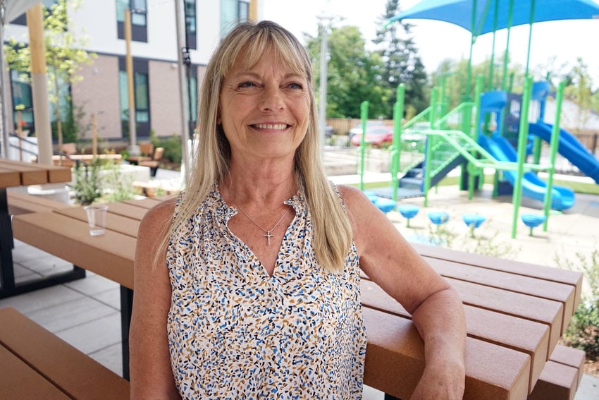 Woman sitting at picnic table in front of play structure, smiling and looking off camera.