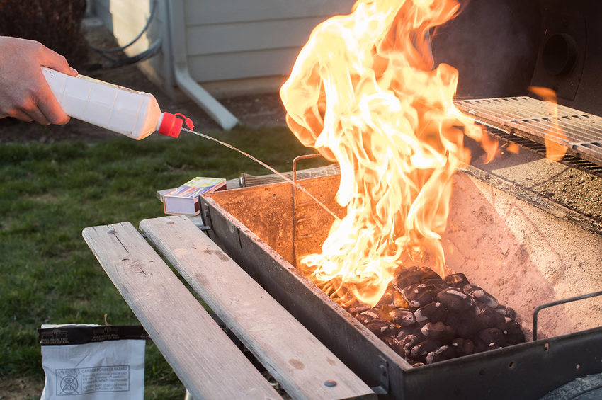 Lighter fluid is squeezed out over an open flame, dousing the charcoal grill and fueling a fire