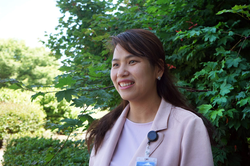 Woman in a pink blazer in front of a leafy bush, smiling and looking off camera.