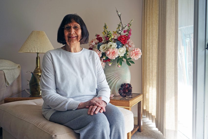 Woman with short dark hair and a white sweatshirt sitting in a livingroom by a glass door.