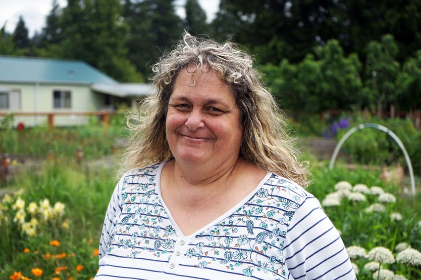 Portrait of a woman with curly blond hair and a floral shirt in a community garden.