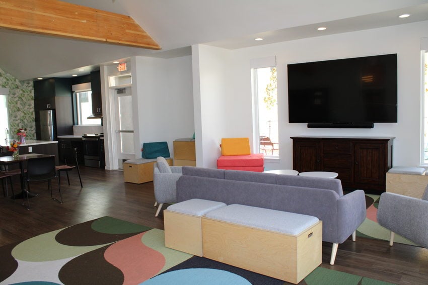 Community room at Las Flores affordable housing project, featuring multi-use furniture, adaptable play couches for children, colorful area rugs, and a large-screen television mounted on the wall.