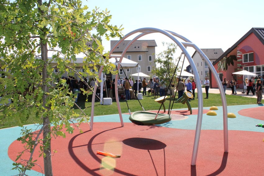 Community playground with an accessible swing and multicolored soft ground surfaces in the heart of Las Flores affordable housing project in Oregon City.