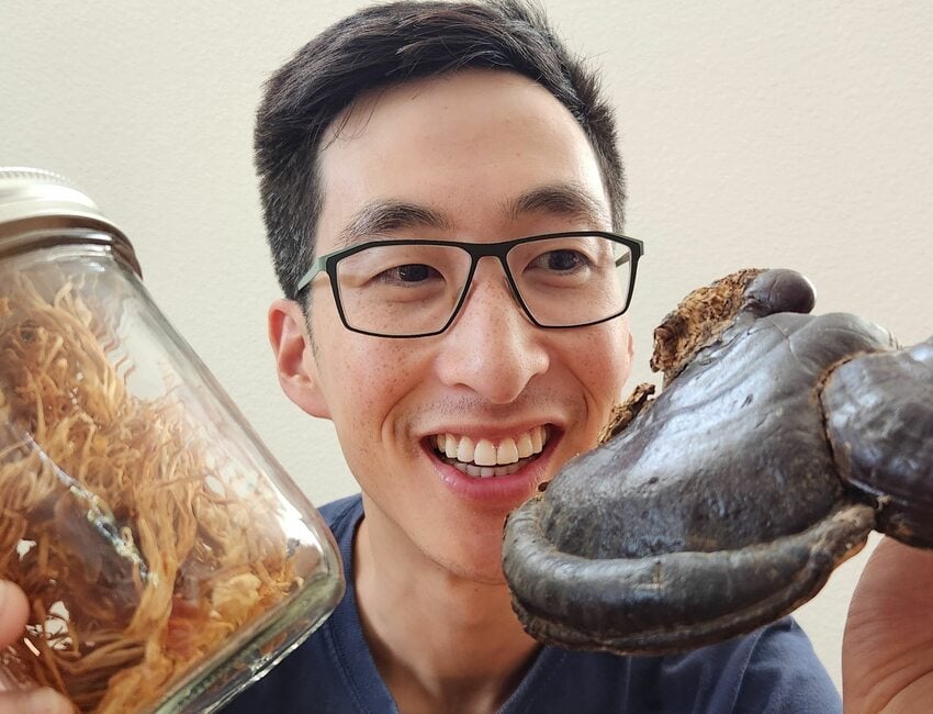 Jeffrey Lee smiles and holds two kinds of fungus up in front of him