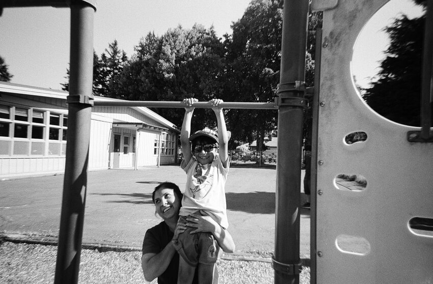 Woman lifing child up onto playground equipment in a school yard.