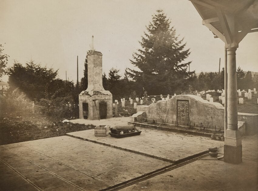 historic sepia-tone photo of a cemetery with a stone altar bearing Chinese writing with sticks of burnt incense. Headstones dot the grass behind the altar, and before it is a large platter bearing a roast pig. To one side is a funerary burner.