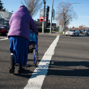 A woman pushes a walker through a crosswalk at 82nd and Powell