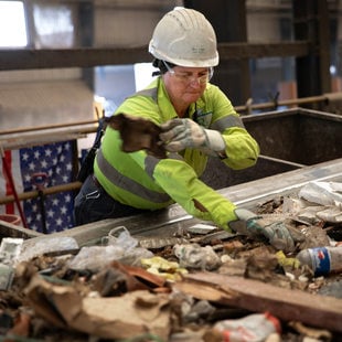 a woman in a hard hat sorts through garbage on a conveyor belt