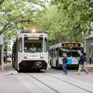 pedestrians cross in front of a MAX train and TriMet bus