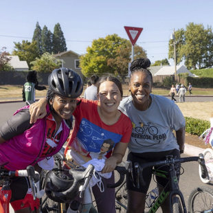 Three adults pause to take a group photo. The adult to the left is wearing a bike helmet and cycling gear.
