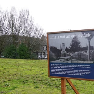 A large sign in a grassy field; the sign has an old photo of a Chinese altar and the words "This is not an empty field"