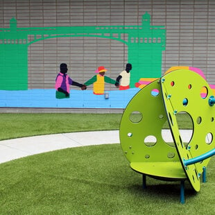 Playground with green structure in foreground and green bridge mural in background.