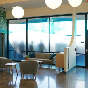 Lobby with frosted gladd windows, murals and stuffed chairs.