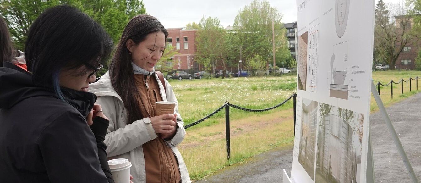 two women stand outdoors looking at informational posters about altar design