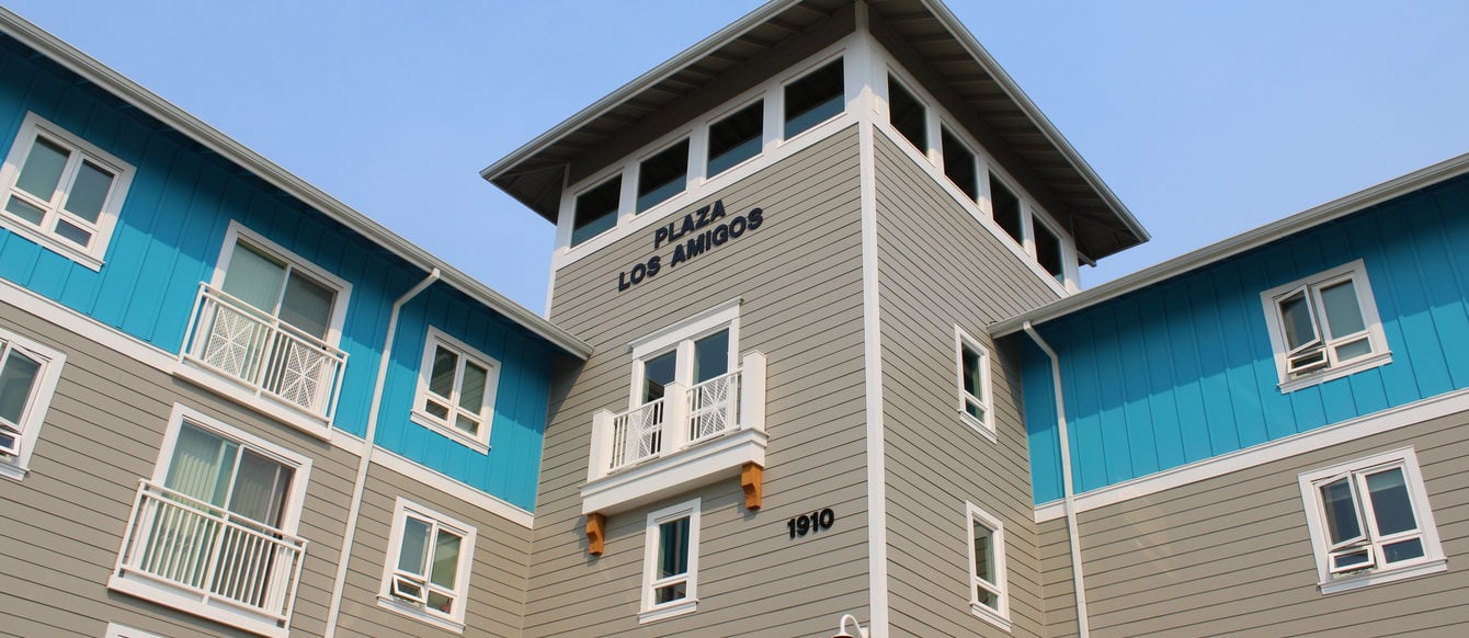 Exterior view of Plaza Los Amigos affordable housing project in Cornelius, a multistory building painted in shades of beige and bright blue.