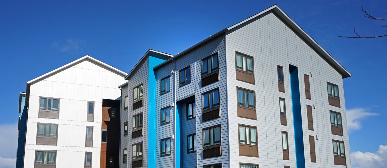 A four-story multifamily building with white, blue and grey exterior finish. 