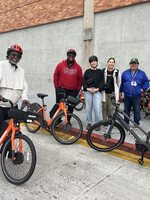 A group of adults with Community Street Trust smile at the camera, standing near a fleet of bicycles. 