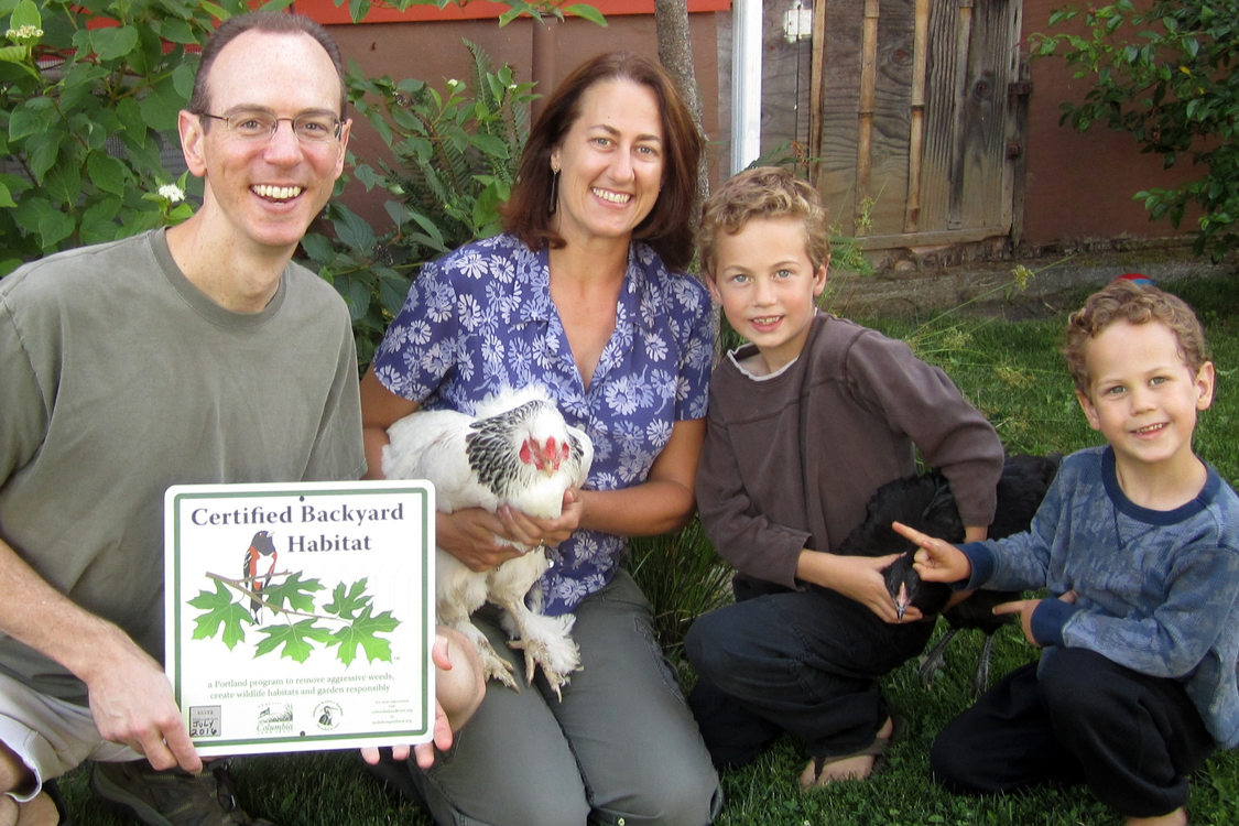 photo of a man holding a Certified Backyard Habitat sign, a woman holding a rooster and two boys holding a chicken