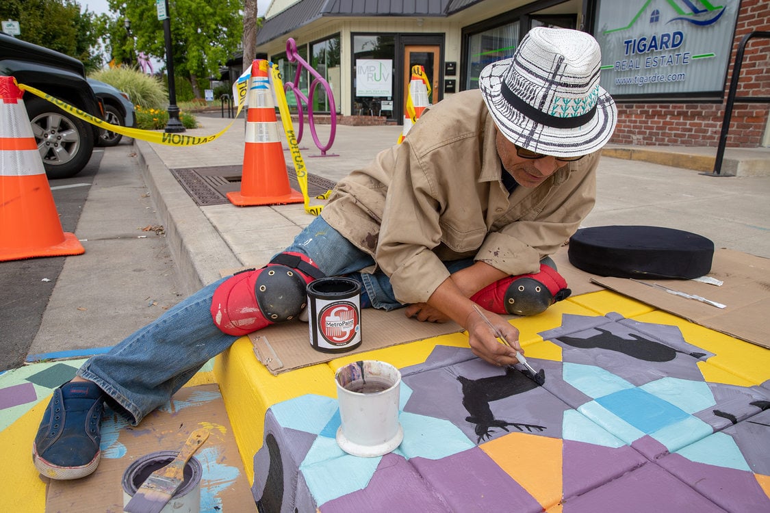 A man paints a mural on the sidewalk in Tigard