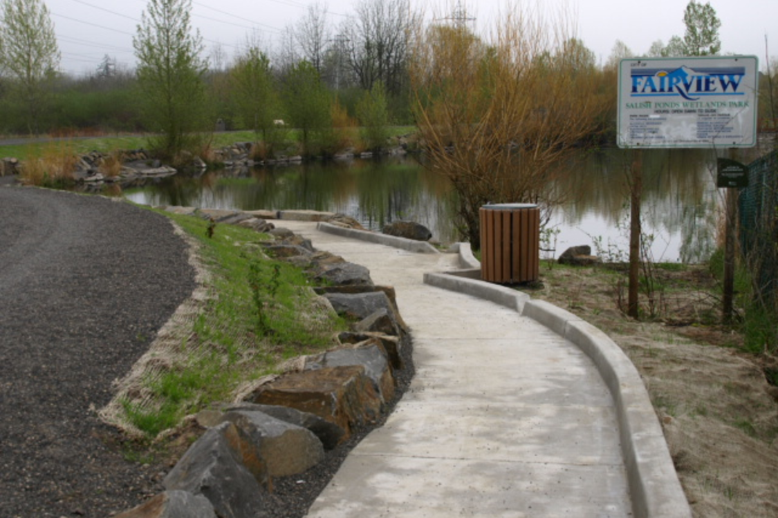Photo of paved trail with pond in background