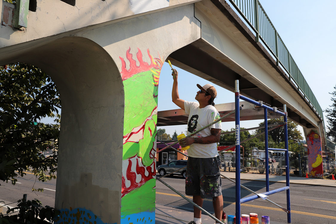 a man paints a mural on the column of a bridge