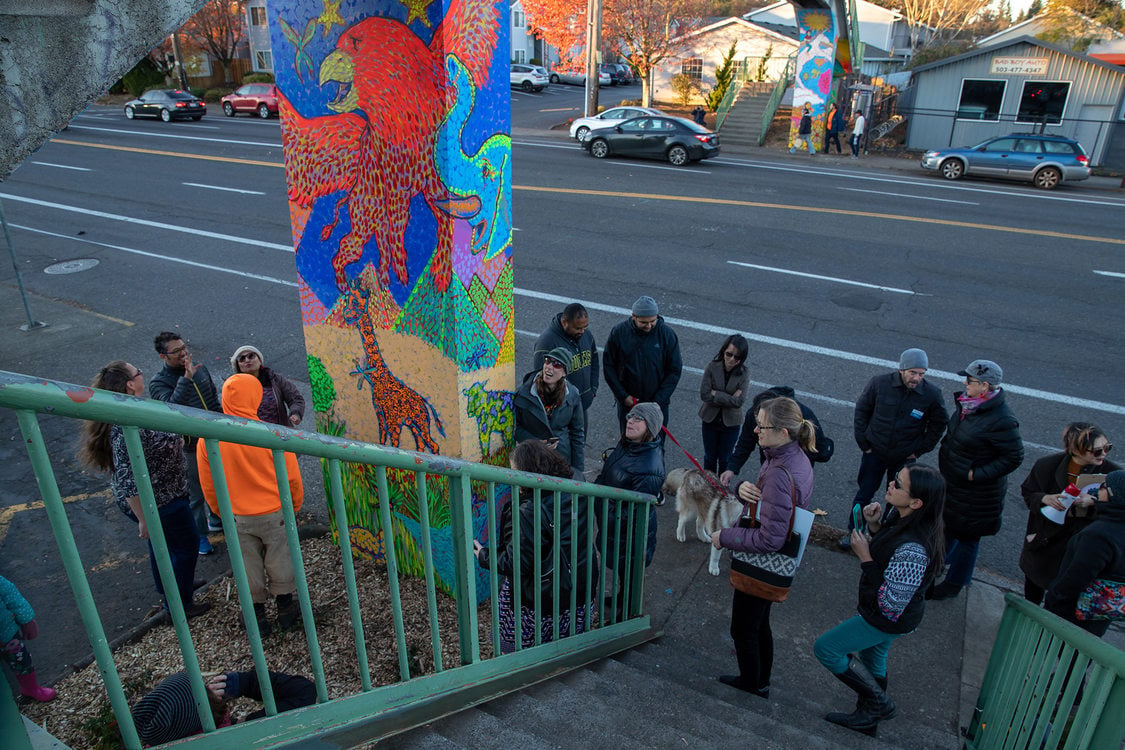 People crowd at the base of a bridge column to check out new mural paintings.
