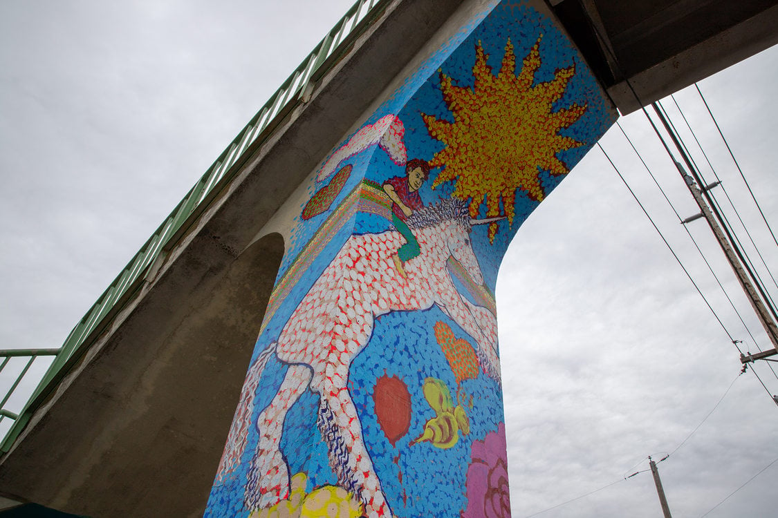 mural painting of a child riding a unicorn; the painting is on the column of a pedestrian bridge