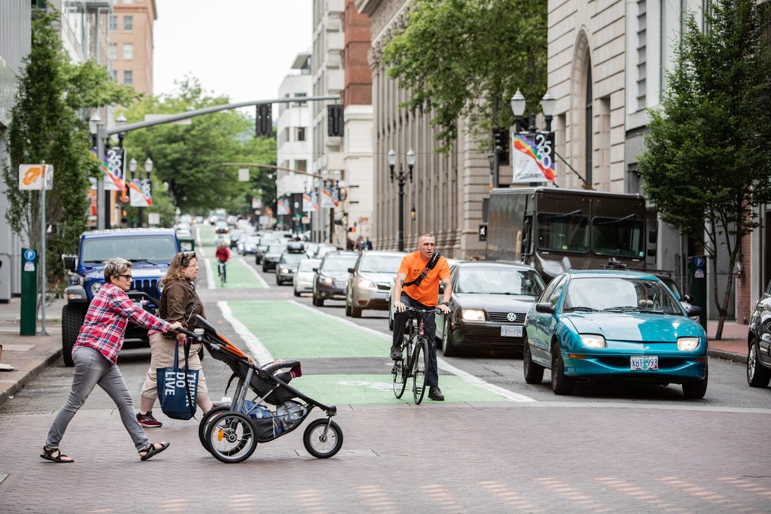 pedestrians cross a street in downtown Portland while a bicyclist and cars wait
