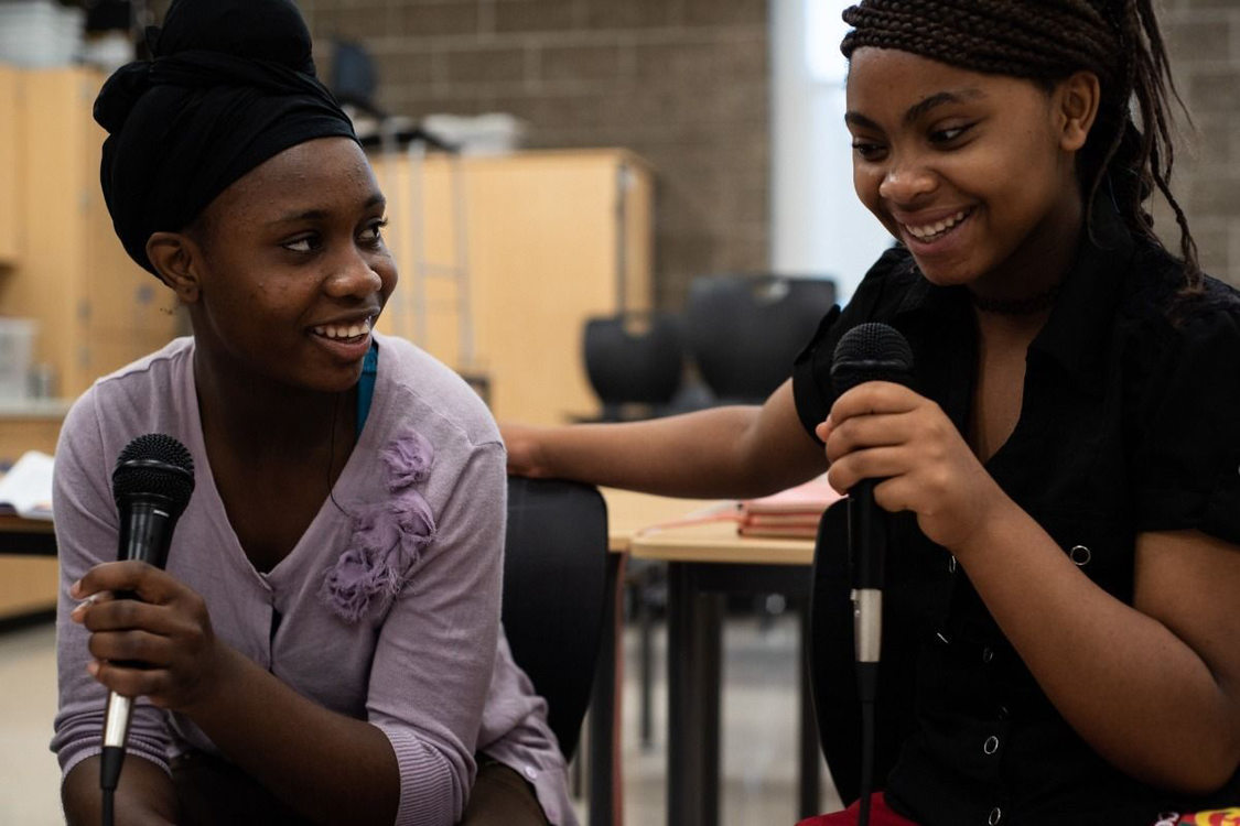two women holding microphones and smiling in a community conversation at Ethos Music Center