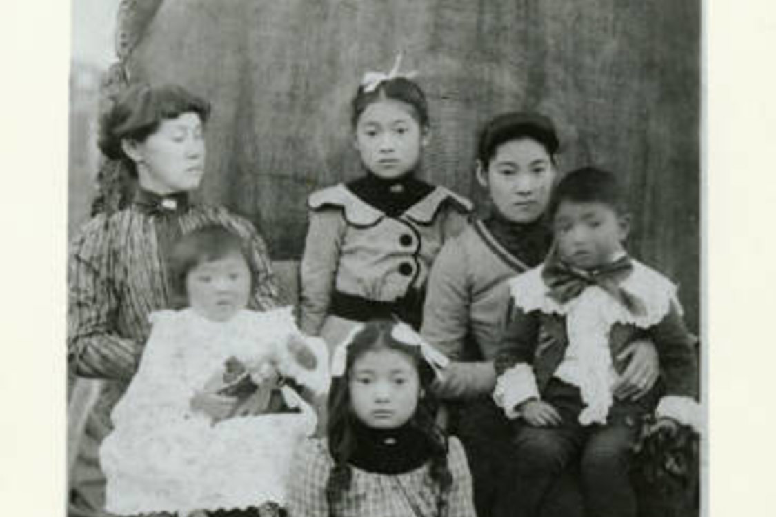 A family of Japanese Americans in formal clothing pose for a photo in front of a huge log. A calico cat hangs out in the foreground.