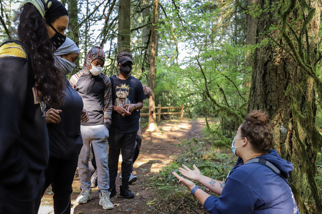 A Metro educator kneels and explains the history of Oxbow Regional Park to standing group of masked people