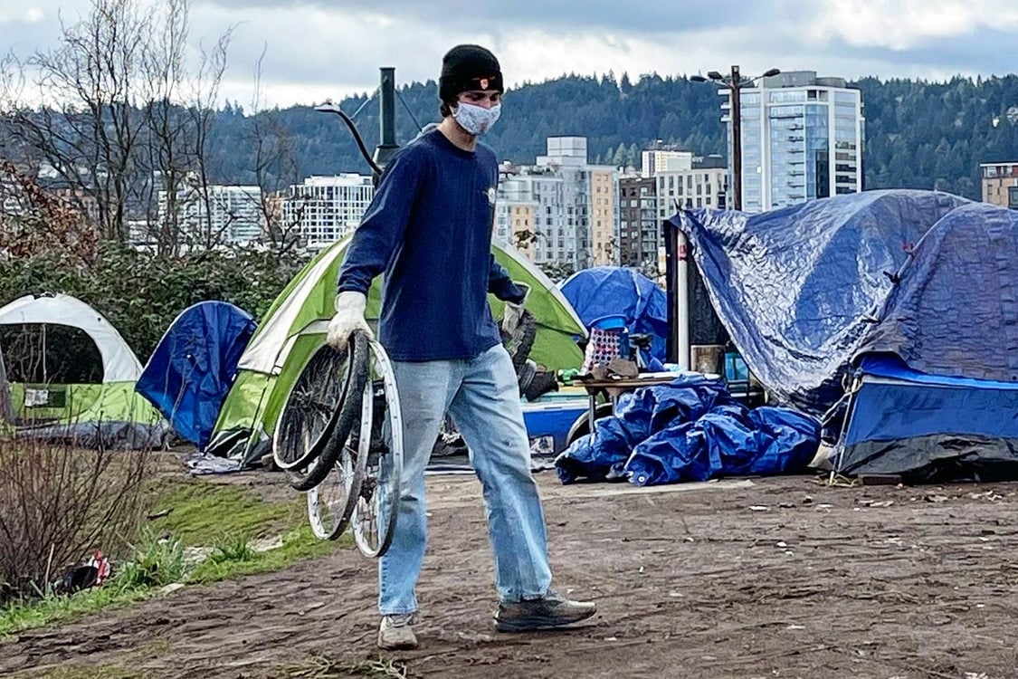 An image of a man carrying bicycle rims in front of tents.