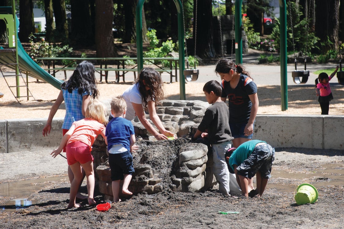A group of children play with water and sand at a play table at a park. 