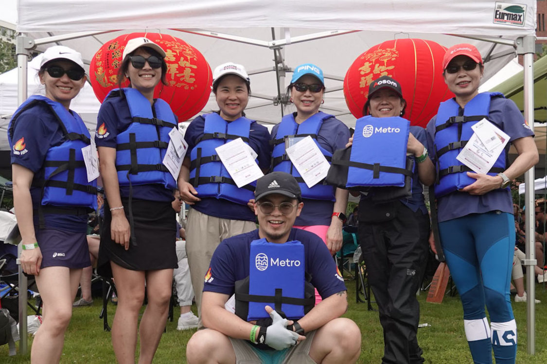 Members of a dragon boat team pose in a line with Metro life jackets, red Chinese-style paper lanterns behind them