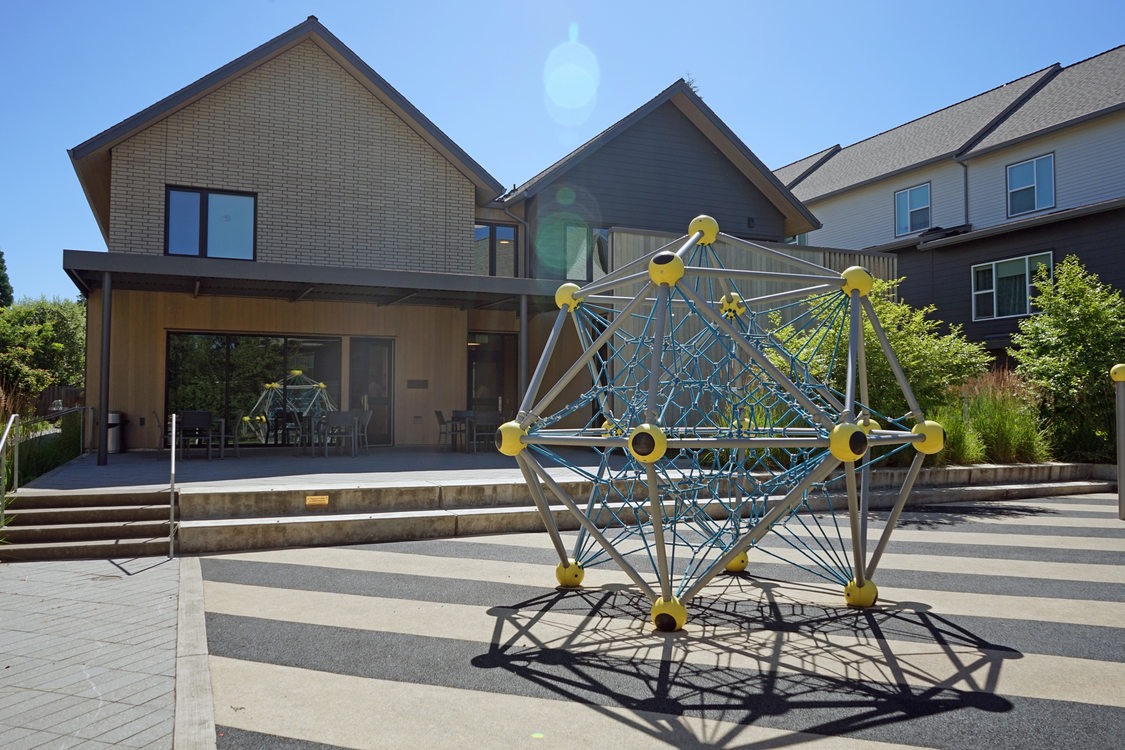 Two-story shelter building with geometric play ground feature in the foreground on a suny day.
