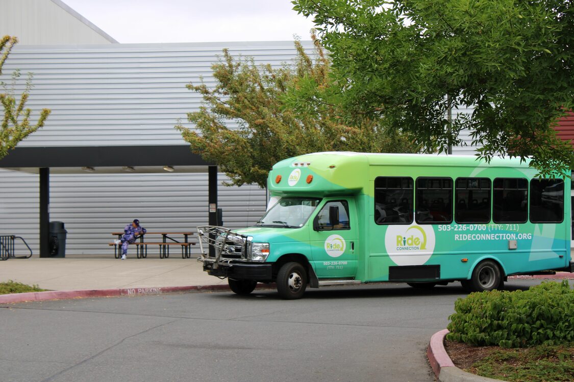 A Ride Connection shuttle bus, painted in shades of green with the Ride Connection logo prominently displayed on the front and sides of the shuttle bus.