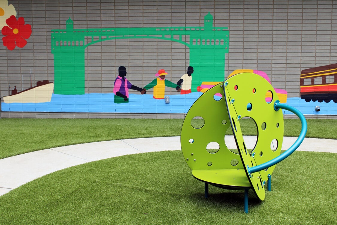 Playground with green structure in foreground and green bridge mural in background.