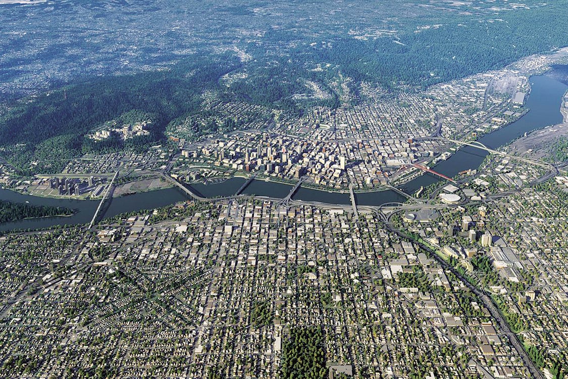 Aerial photo of downtown Portland looking west, with the Willamette River running across from left to right. The street grid and many major bridges across the river are visible.