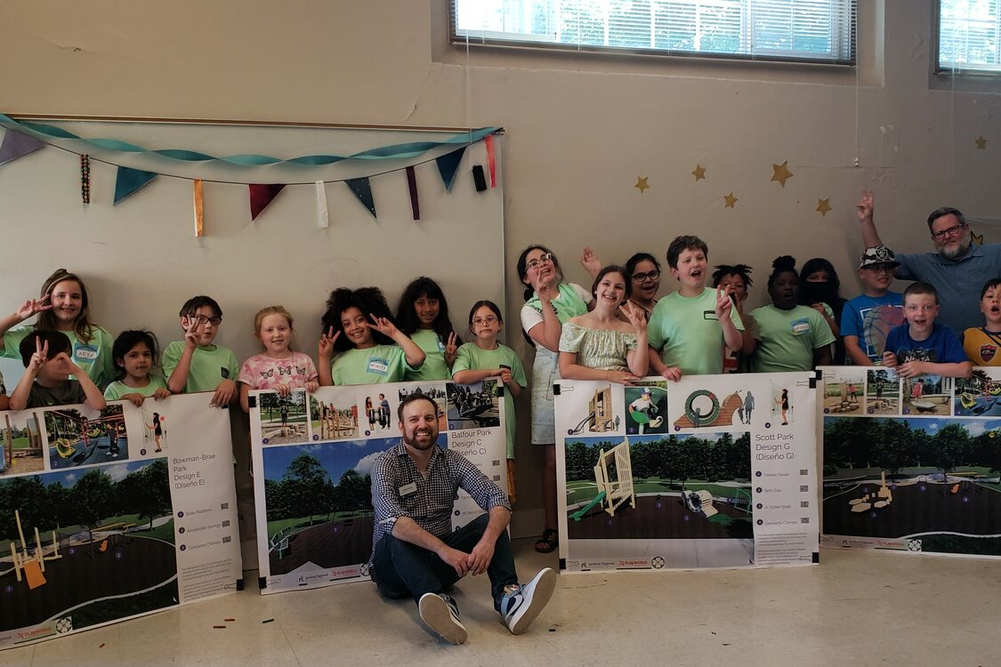 A large group of children hold up posters with designs for the city’s remaining undeveloped neighborhood parks.