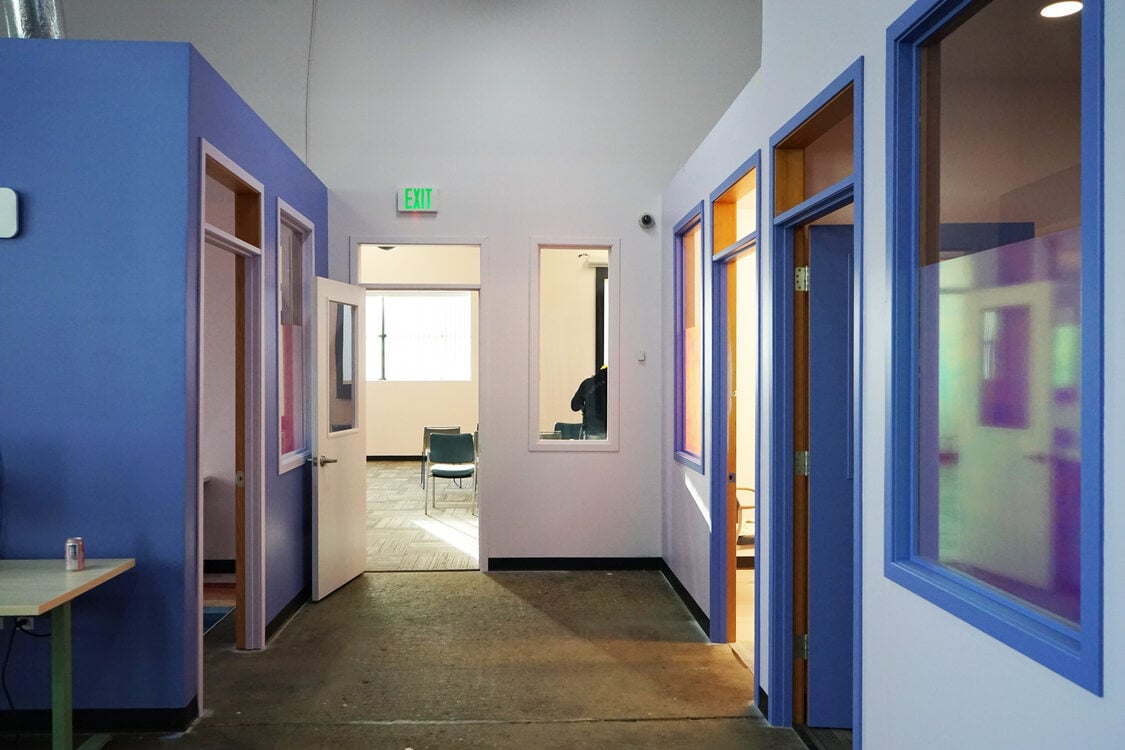 Office hallway with purple and lavender walls, leading to a large, light-filled room.