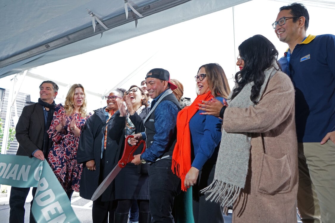 A diverse group of individuals gathered around a large ribbon, preparing to cut it during a ceremonial event.