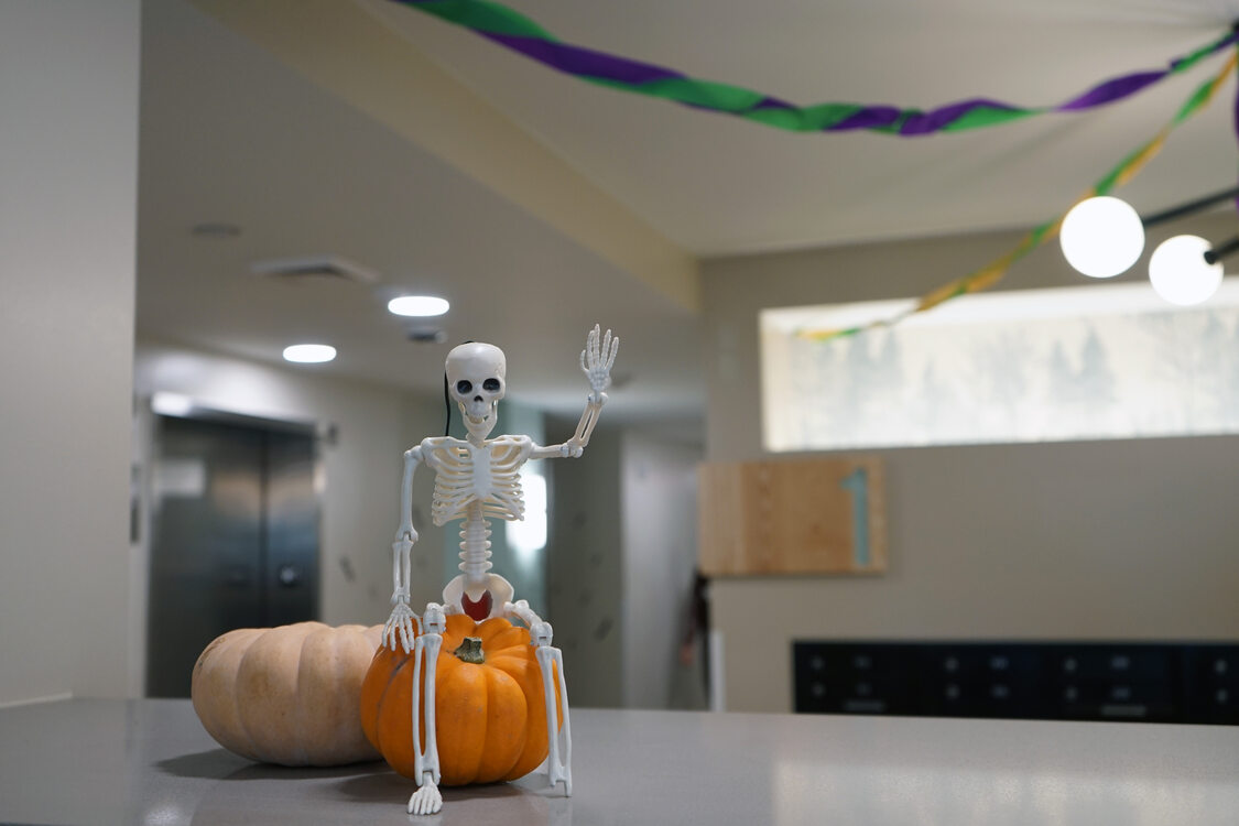 Plastic skeleton sitting on a tiny pumpkin waving "hello"