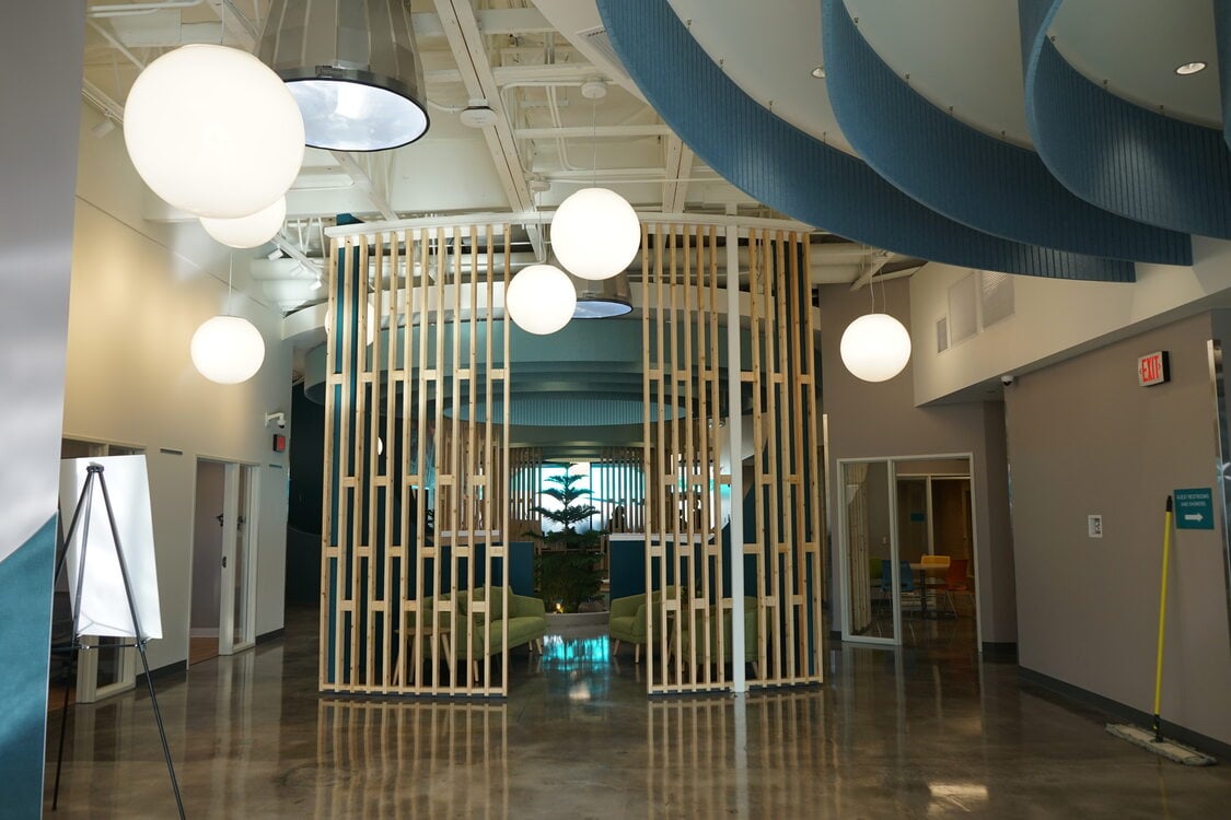 Lobby with rounded wood screen, round hanging lamps and a tree in the center.